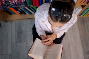 Woman reading open book next to shelves of books