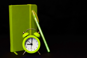 Green sketchbook, pencil, and alarm clock on black background