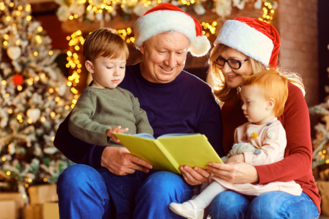 Two adults in Santa hats reading a book to two young children