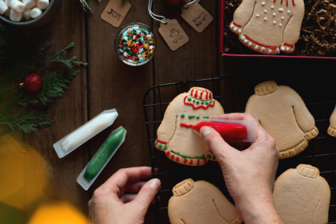 Hand decorating a cookie shaped like a holiday sweater