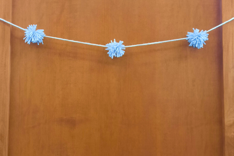 Blue pompom garland draped across wooden wall.