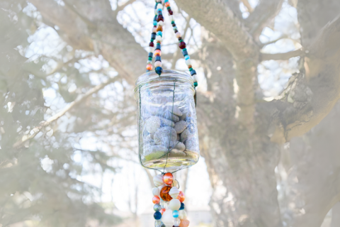 Clear jar of stones hanging from a tree branch with beaded decoration above and below