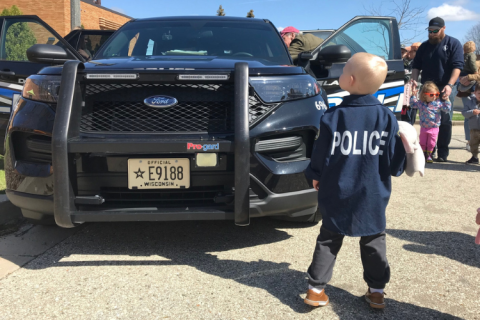 Child wearing a police jacket looking at a Delafield Police car