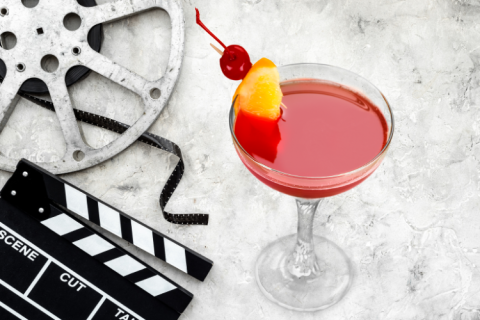 Red drink garnished with fruit next to black and white film reel