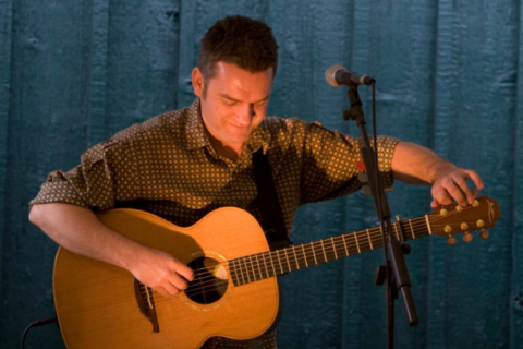 Musician Ian Gould tuning an acoustic guitar