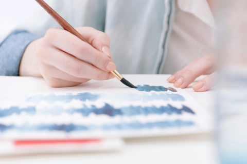 Close-up of hand painting blue streaks on a canvas