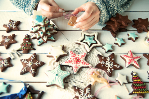 A table of frosted and decorated Christmas cookies and two hands decorating them