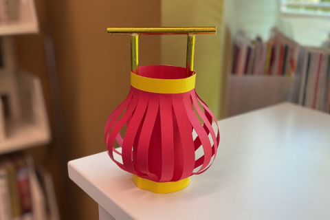 Round red lantern made of paper with a gold handle.