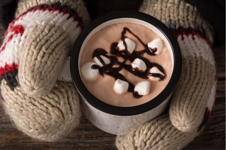 Mittened hands holding mug of hot cocoa with marshmallows.