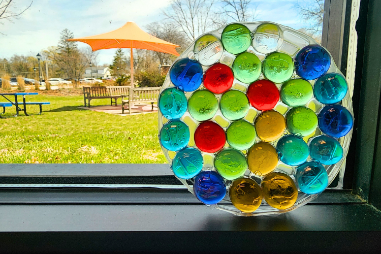 Round suncatcher made from colorful flat marbles in a window
