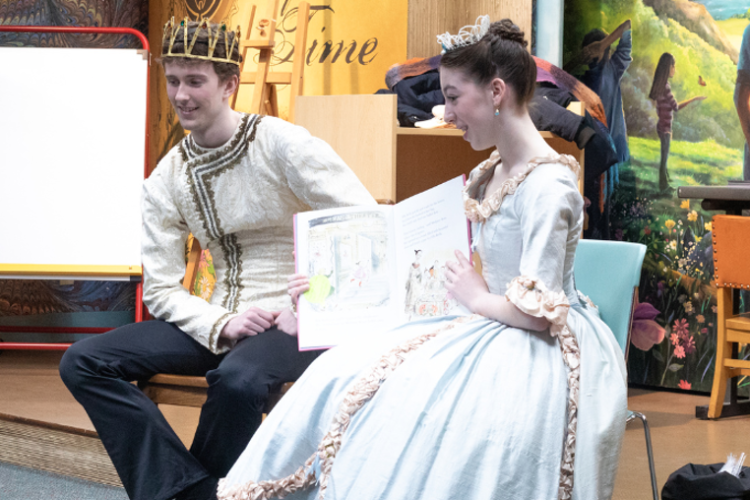 Two ballet dancers dressed as prince and princess reading a story