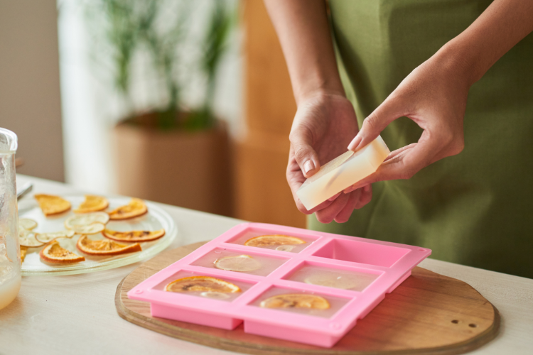 A woman removing homemade soap bars from a pink tray.