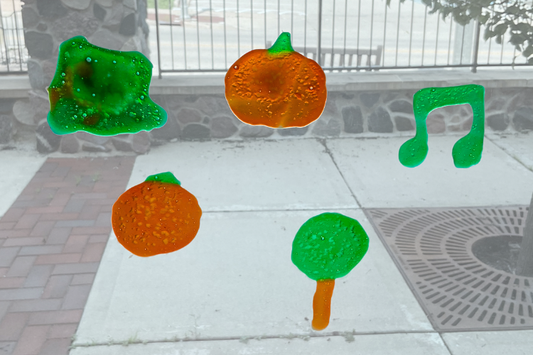 Squishy orange and green clings on a window in the shape of pumpkins, trees, and music notes.