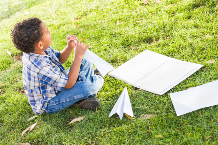 Child on grass folding paper into airplanes.