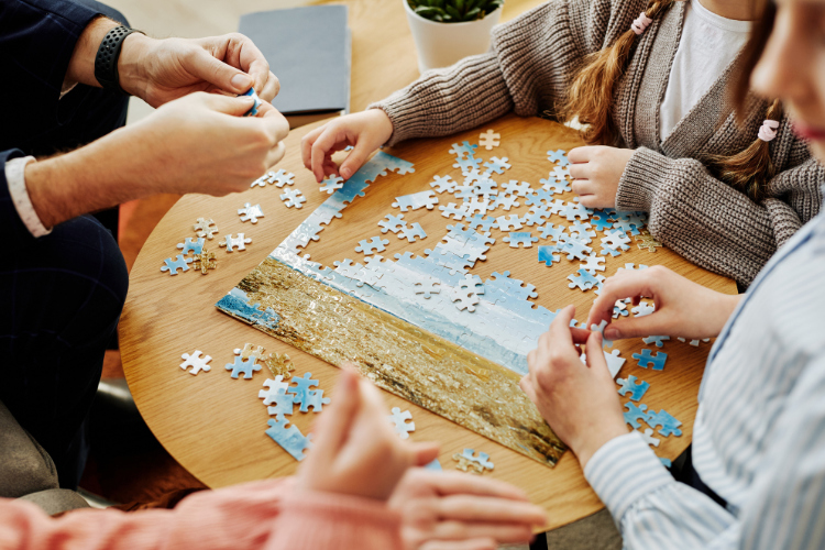 Four sets of hands putting a puzzle together on a wooden table