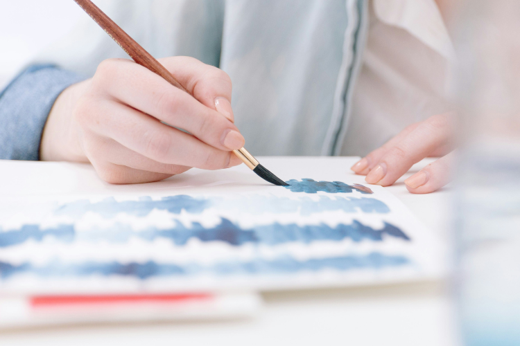 Close-up of hand painting blue streaks on a canvas