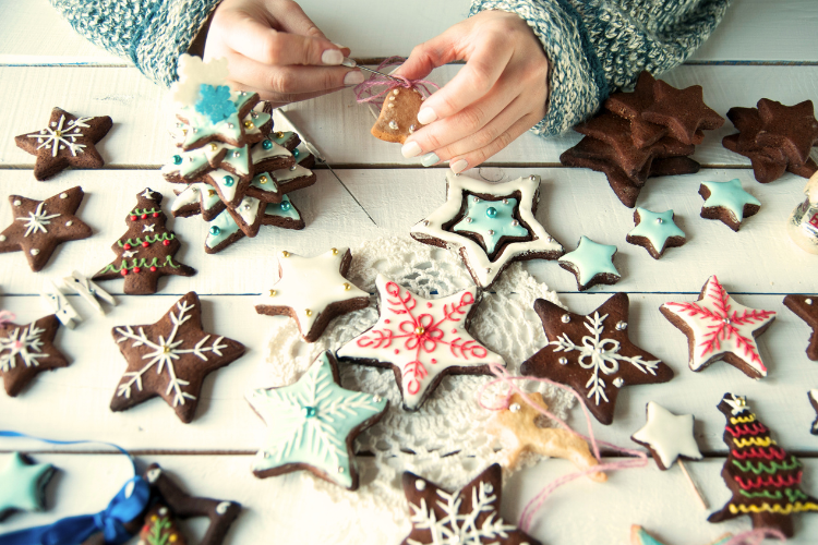 A table of frosted and decorated Christmas cookies and two hands decorating them