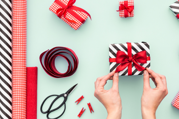 Two hands tying a red bow on a black and white striped gift.
