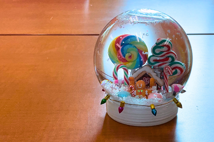 A clear snow globe filled with a gingerbread man and colorful candy accessories