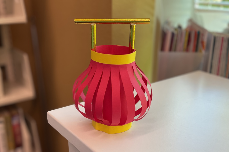 Round red lantern made of paper with a gold handle.
